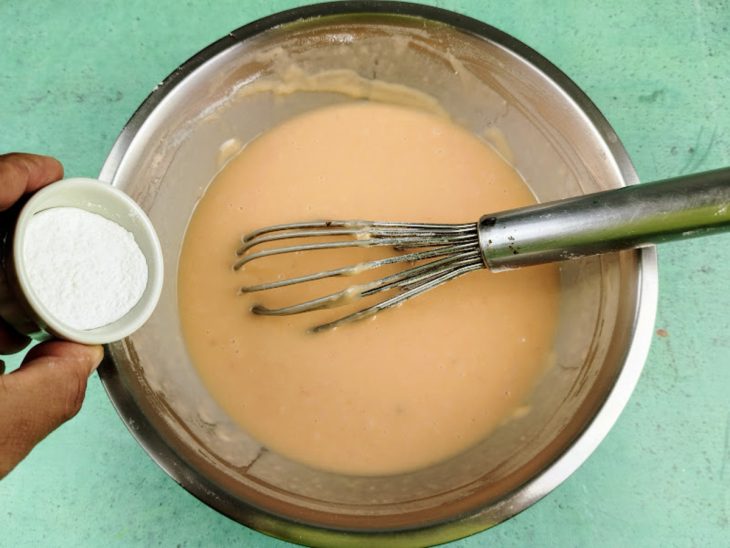 uma vasilha redonda com a mistura da massa com um batedor de arame e uma vasilha redonda menor com o fermento em pó.