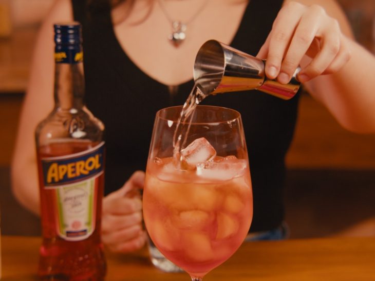 Uma taça contendo a mistura de gelo, espumante, aperol e água com gás.