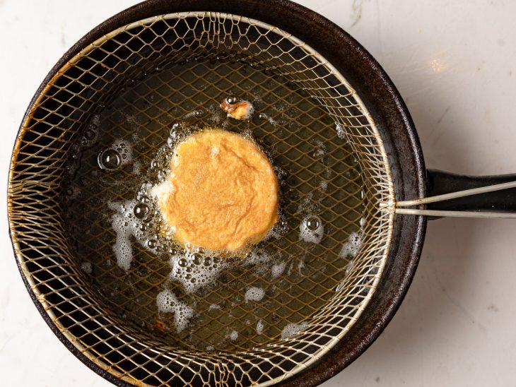 Arepa recheada sendo frita por imersão em uma panela com óleo.