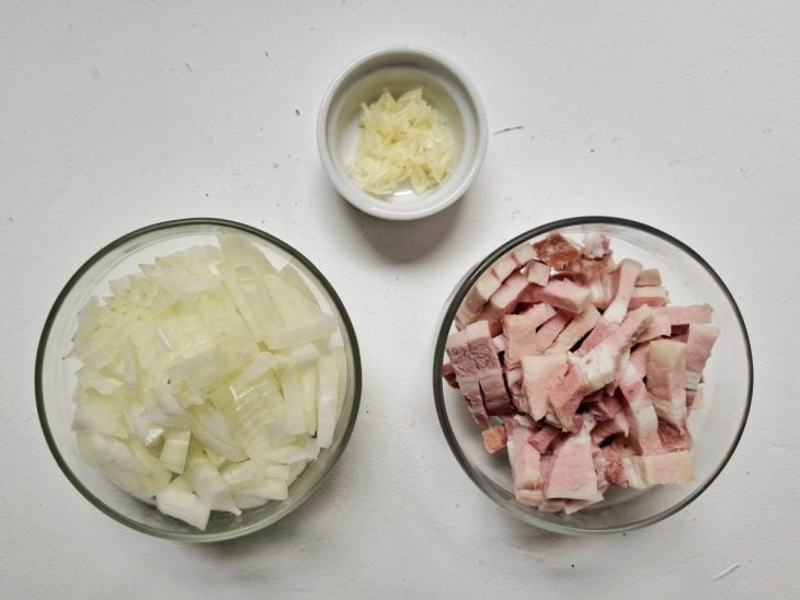 Cebola, alho e bacon cortados e separados em recipientes.