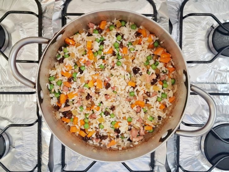 Panela com legumes, arroz, passas brancas e escuras misturados.