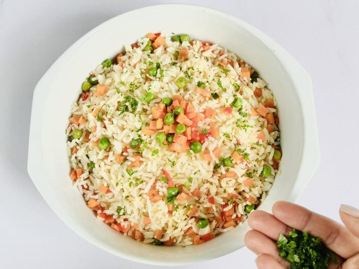 Arroz à grega com cenoura finalizado e sendo acrescentado cheiro verde