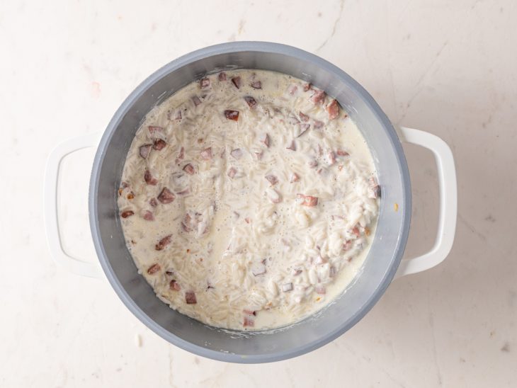 panela com arroz cozido, cubinhos de calabresa, creme de leite e temperos