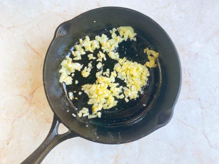 Alho e cebola refogados na manteiga em uma frigideira.