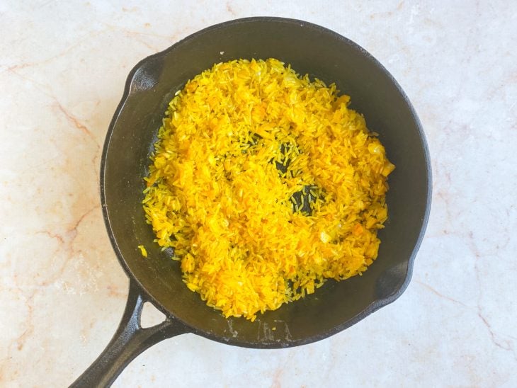 Arroz e açafrão adicionados a frigideira com alho e cebola.