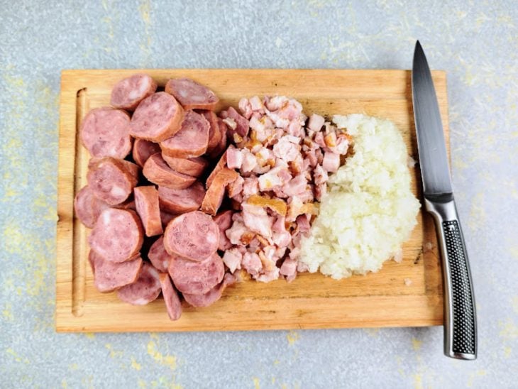 Calabresa, Bacon, Cebola e alho picados em uma tabua de madeira.