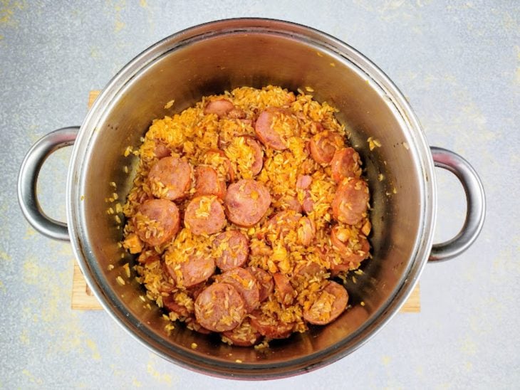 Cebola, alho, açafrão, colorau e arroz adicionados a calabresa e ao bacon na panela.