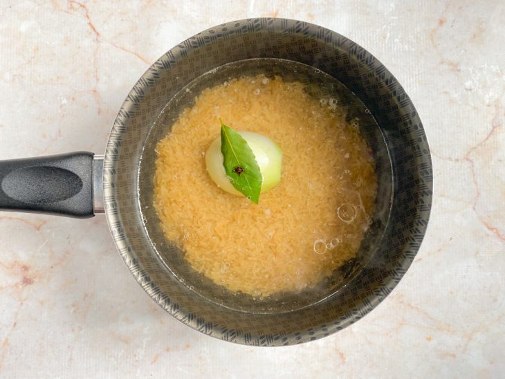 Uma panela com arroz, azeite, água, cebola piqué e temperos.