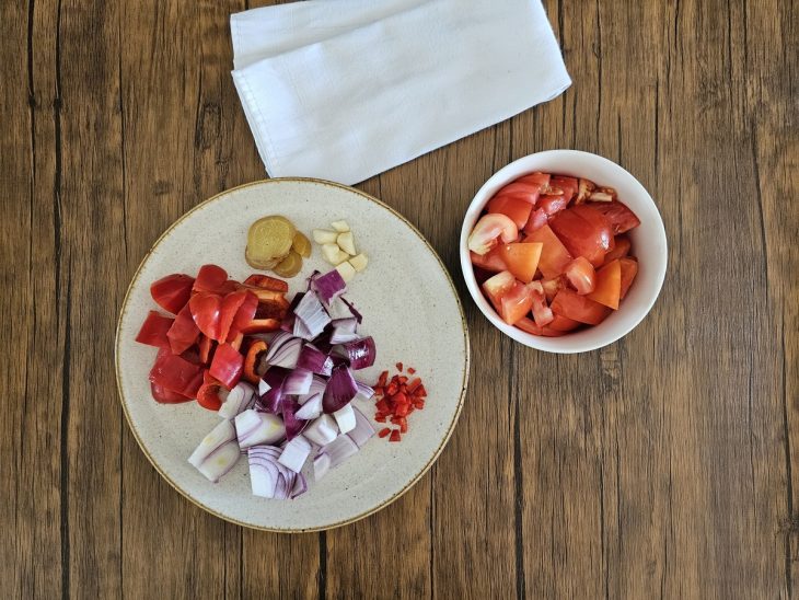 Recipientes com cebola, pimentão, gengibre, alho, tomates e pimenta picados.