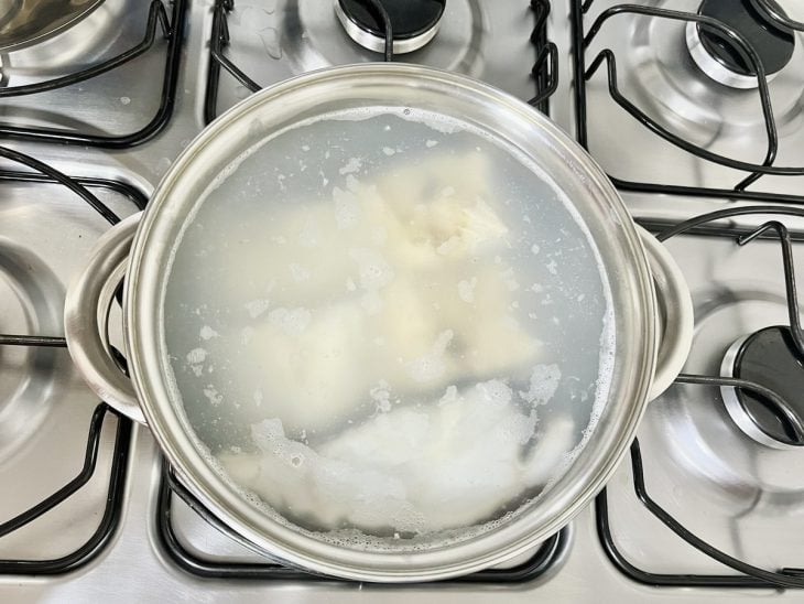 Uma panela com água e postas do bacalhau ao fogo.