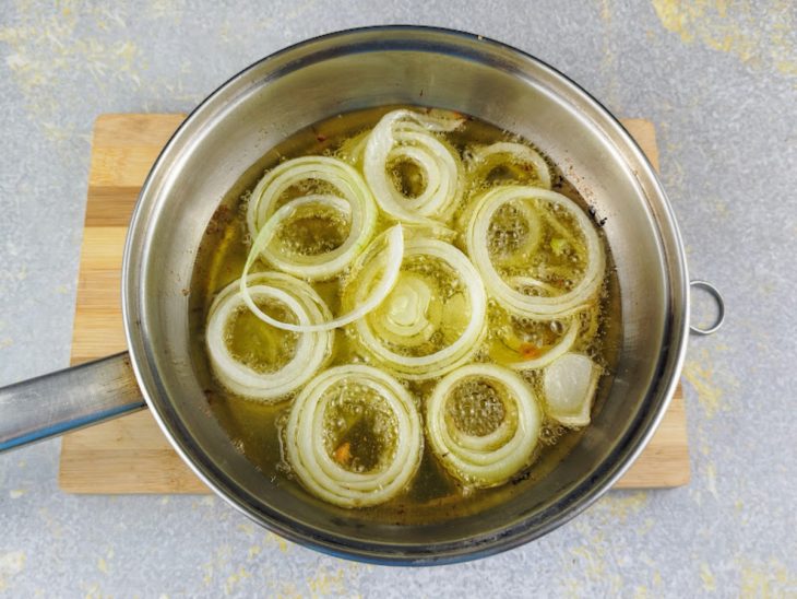 Rodelas de cebola fritando em uma frigideira com azeite.