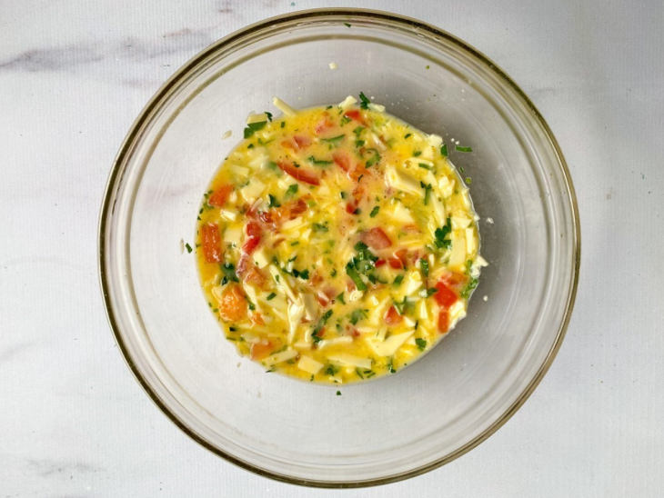 tigela com ovo batido, queijo ralado, tomate e salsinha