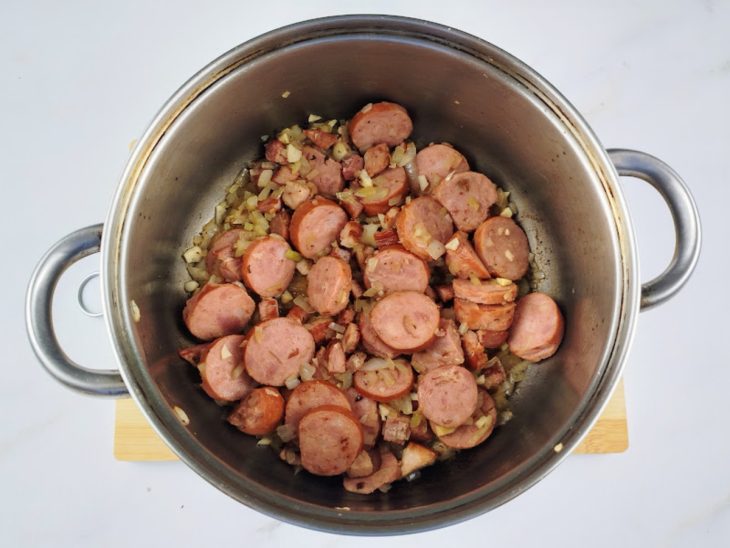 Cebola, alho, manteiga e carne seca adicionados na panela com bacon e calabresa.