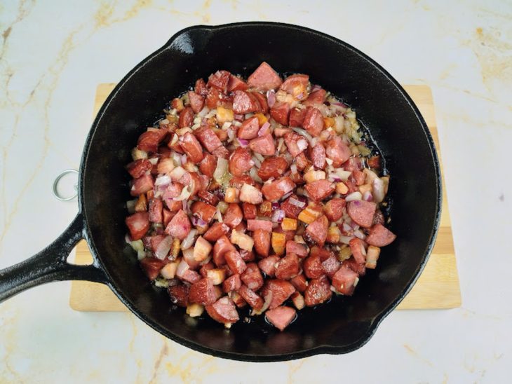 Uma frigideira com bacon, calabresa, cebola e alho.