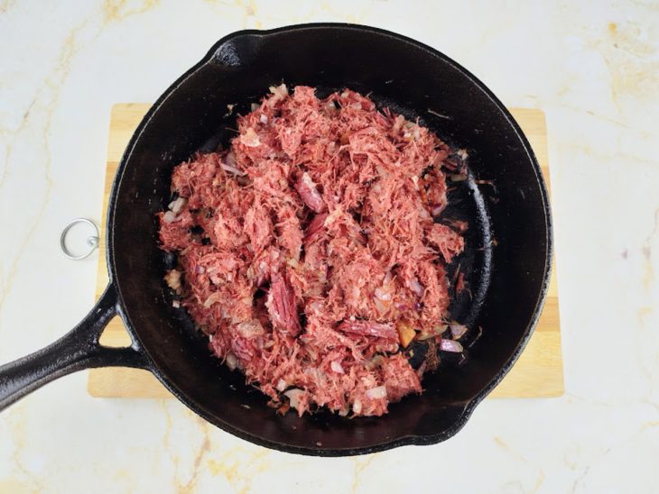 Uma frigideira com carne seca e a cebola refogando.