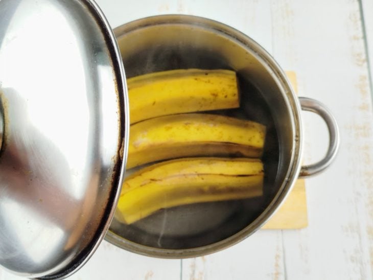 Uma panela com água e bananas sendo tampada.