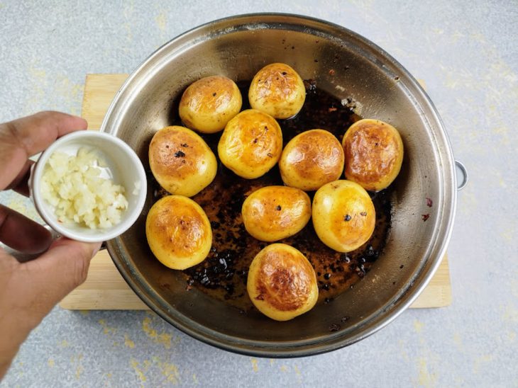 Frigideira com batatas douradas e recipiente com alho para ser adicionado