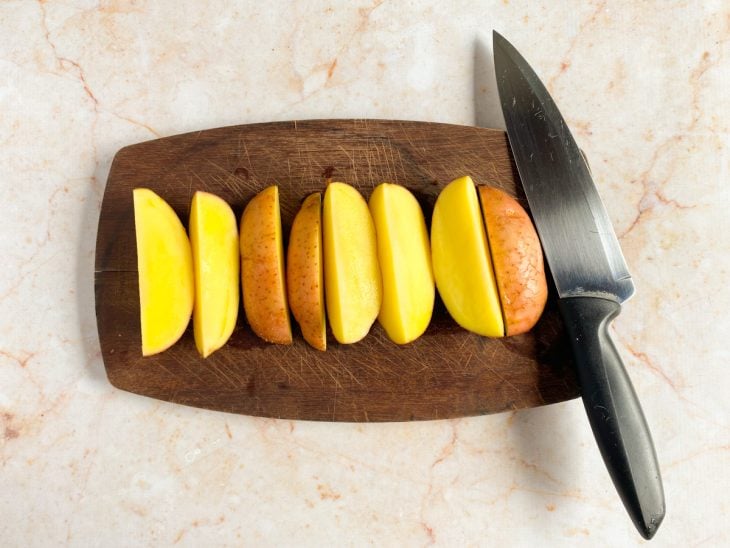 Batatas cortadas em uma tabua de madeira.