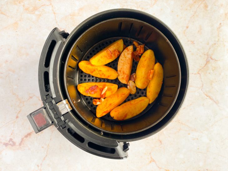 Batatas picadas e temperadas espalhadas dentro da air fryer.