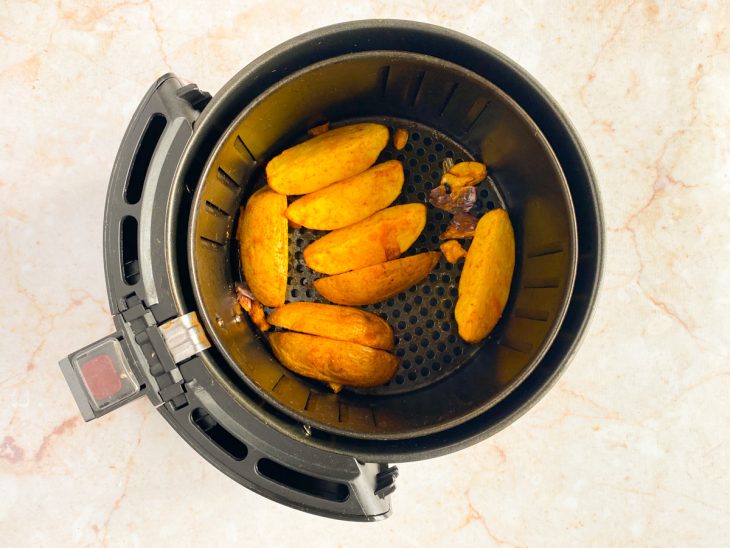 Batatas picadas sendo viradas dentro da air fryer.