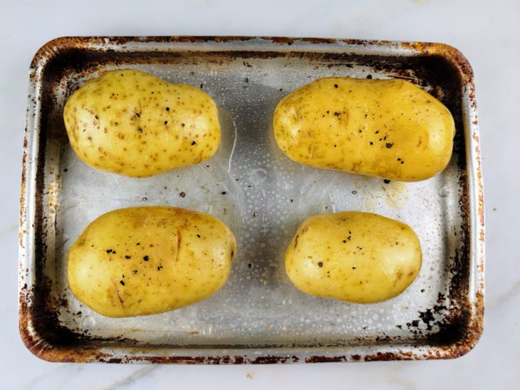 Batatas com azeite e temperos acomodadas em uma forma.