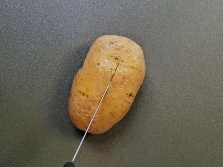 Uma batata sendo cortada com uma faca sobre a tábua.