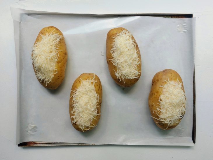 Uma assadeira com batatas recheadas e queijo.
