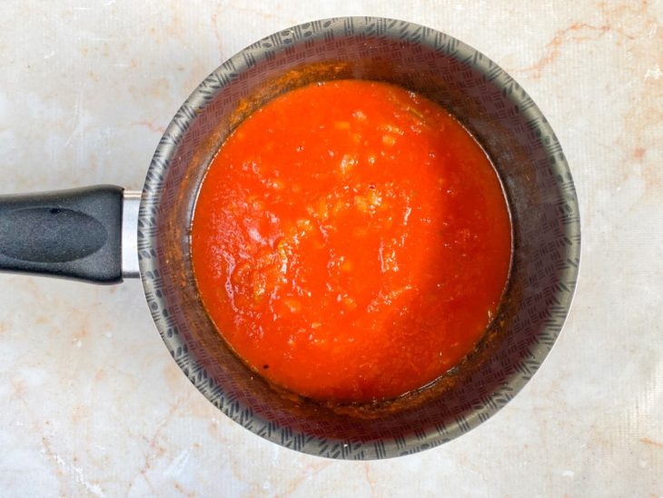 Molho de tomate, sal e pimenta-do-reino adicionados na panela com cebola dourada.