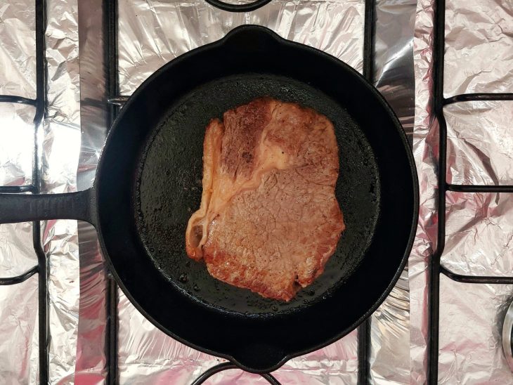 Uma frigideira selando um bife ancho.