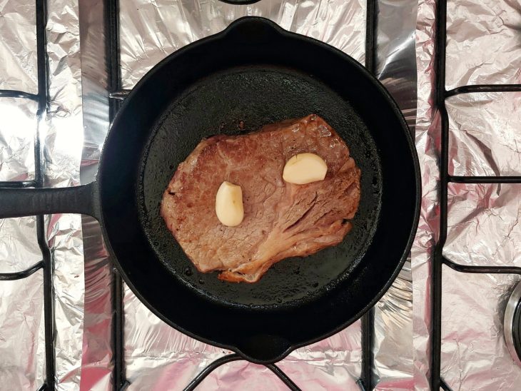 Uma frigideira selando um bife ancho com dentes de alho.