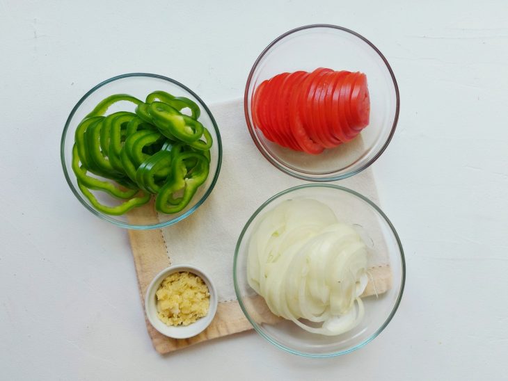 Recipientes com pimentão, alho, cebola e tomate fatiados.