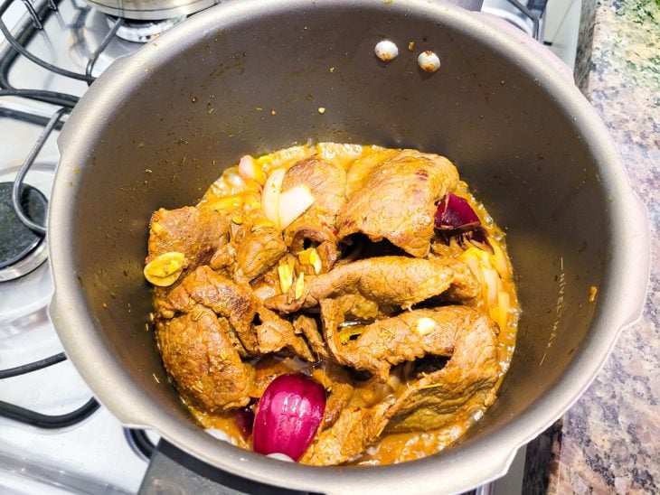 Uma panela de pressão refogando bifes, cebolas e água.