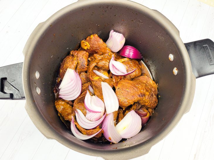 Uma panela de pressão refogando bifes, cebolas e água.