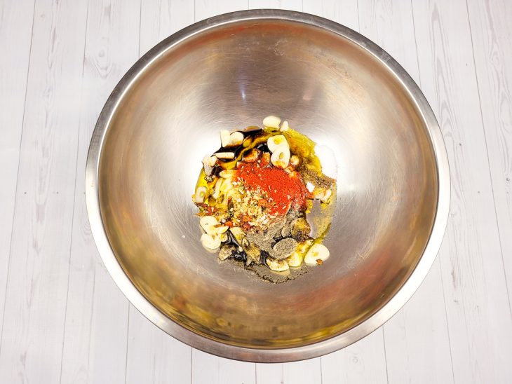 Um recipiente contendo alho picado, shoyu, páprica, pimenta calabresa, sal, pimenta-do-reino e azeite.