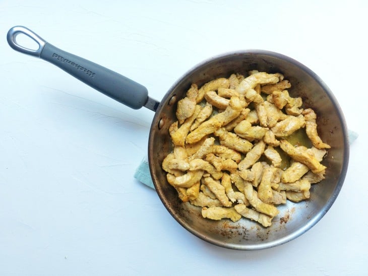 Uma frigideira contendo bistecas de porco em tirinhas fritas.