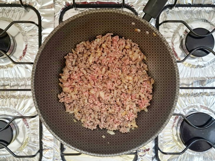 Cebola, alho e carne moída colocados na frigideira com azeite quente.