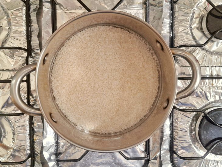 Panela ao fogo com água e arroz cozinhando.