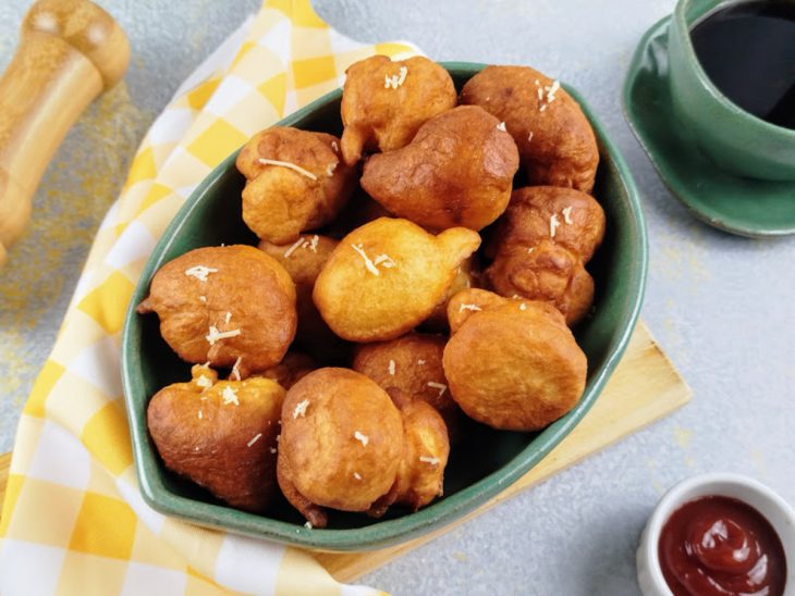 Bolinhos de chuva salgado fritos servidos em um recipiente de cor esverdeada.