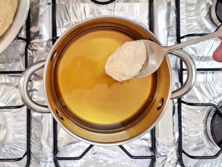 Panela com óleo e uma colher com uma porção da massa de bolinho de chuva.