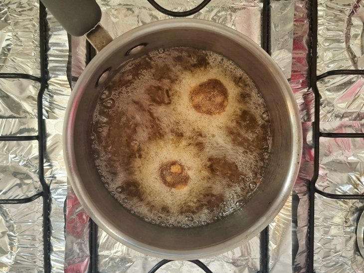 Uma panela com óleo quente e bolinhos fritando.