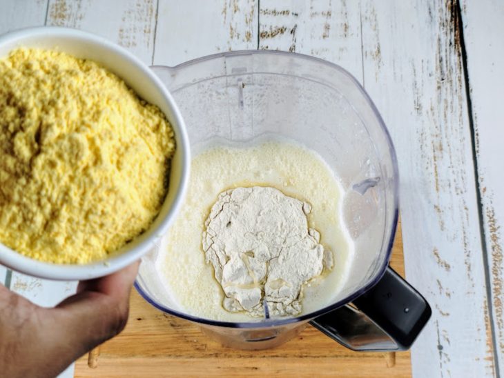 Um liquidificador com a mistura de ovos, leite, manteiga, açúcar, leite condensado, fubá e farinha.