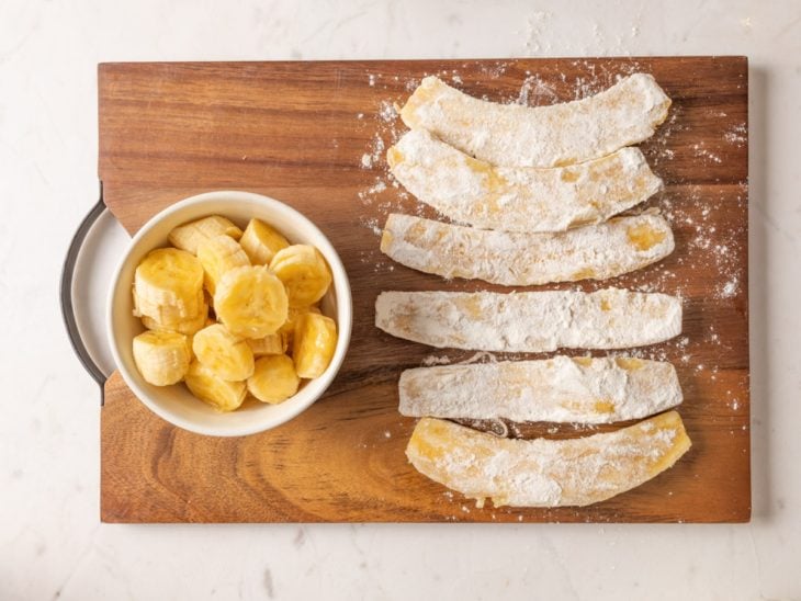 Uma tábua com bananas descascadas, fatiadas e enfarinhadas.