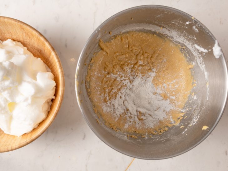 Uma tigela com claras e outra com a mistura de gemas, manteiga, açúcar demerara, baunilha, farinha de amêndoas, farinha de arroz e fermento.