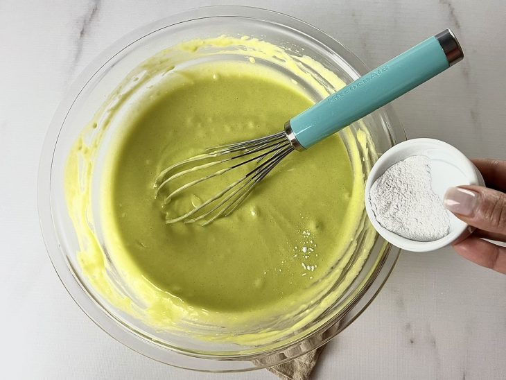 Tigela com farinha e mistura do liquidificador incorporadas. E fermento em um recipiente para ser adicionado.