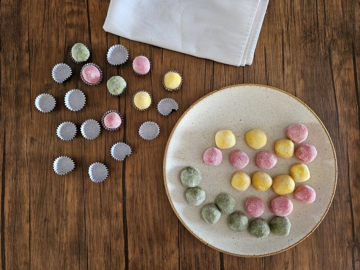 Brigadeiros coloridos com corantes sendo enrolados.