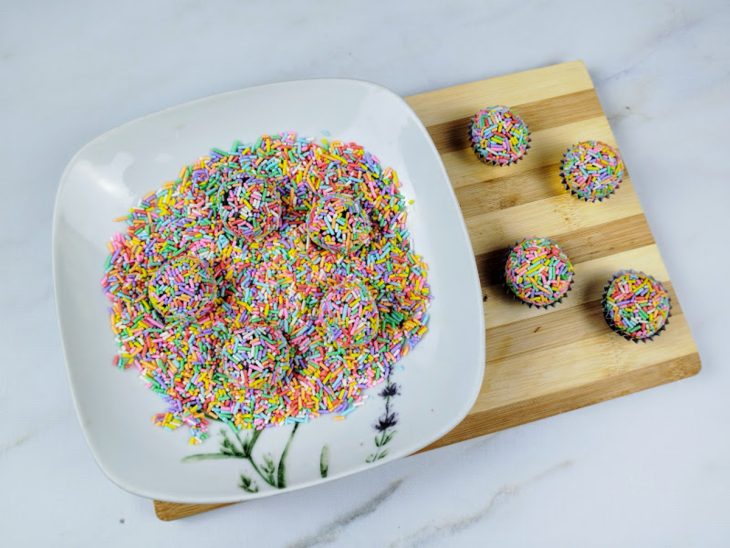 Um prato contendo chocolate granulado e bolinhas de brigadeiro.