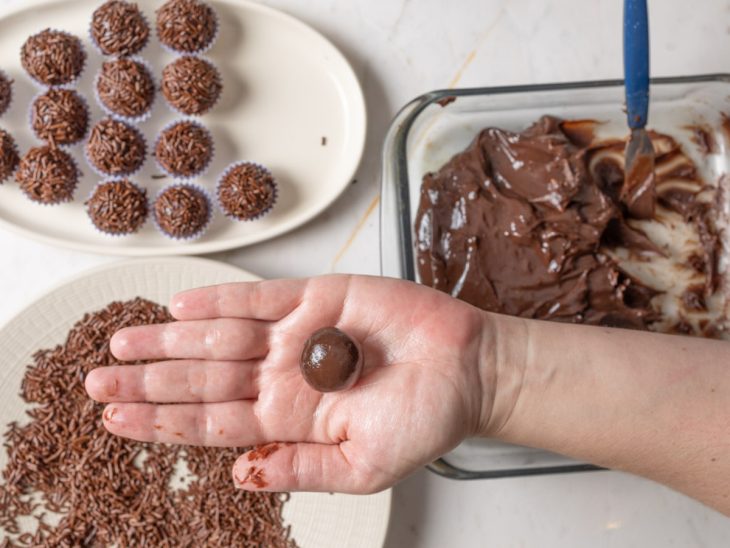 Brigadeiros sendo enrolados e confeitados com granulado.