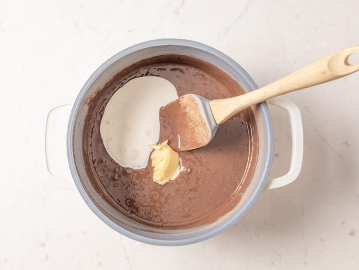 Creme de leite e manteiga adicionados a mistura de leite condensado e chocolate em pó.