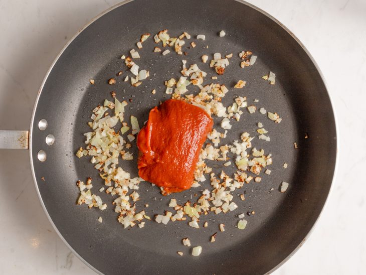 Alho, cebola e extrato de tomate em uma frigideira.