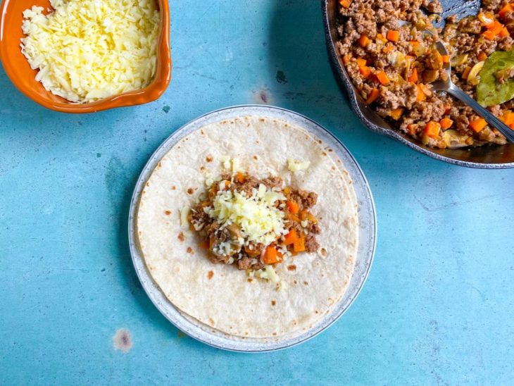 Um prato com uma tortilha, com o recheio de carne moída temperada junto com queijo ralado no meio.